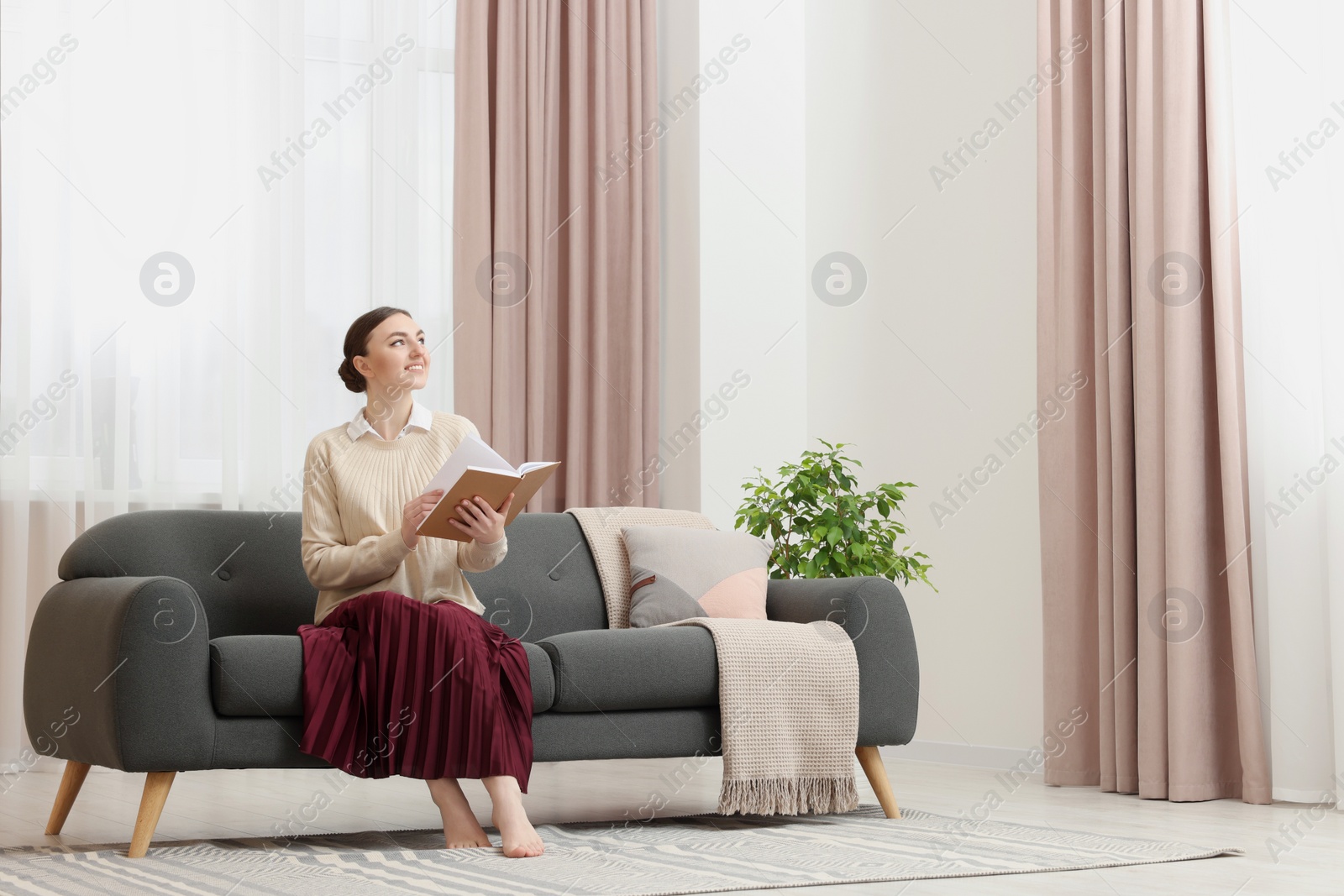 Photo of Woman reading book on sofa near window with stylish curtains at home. Space for text