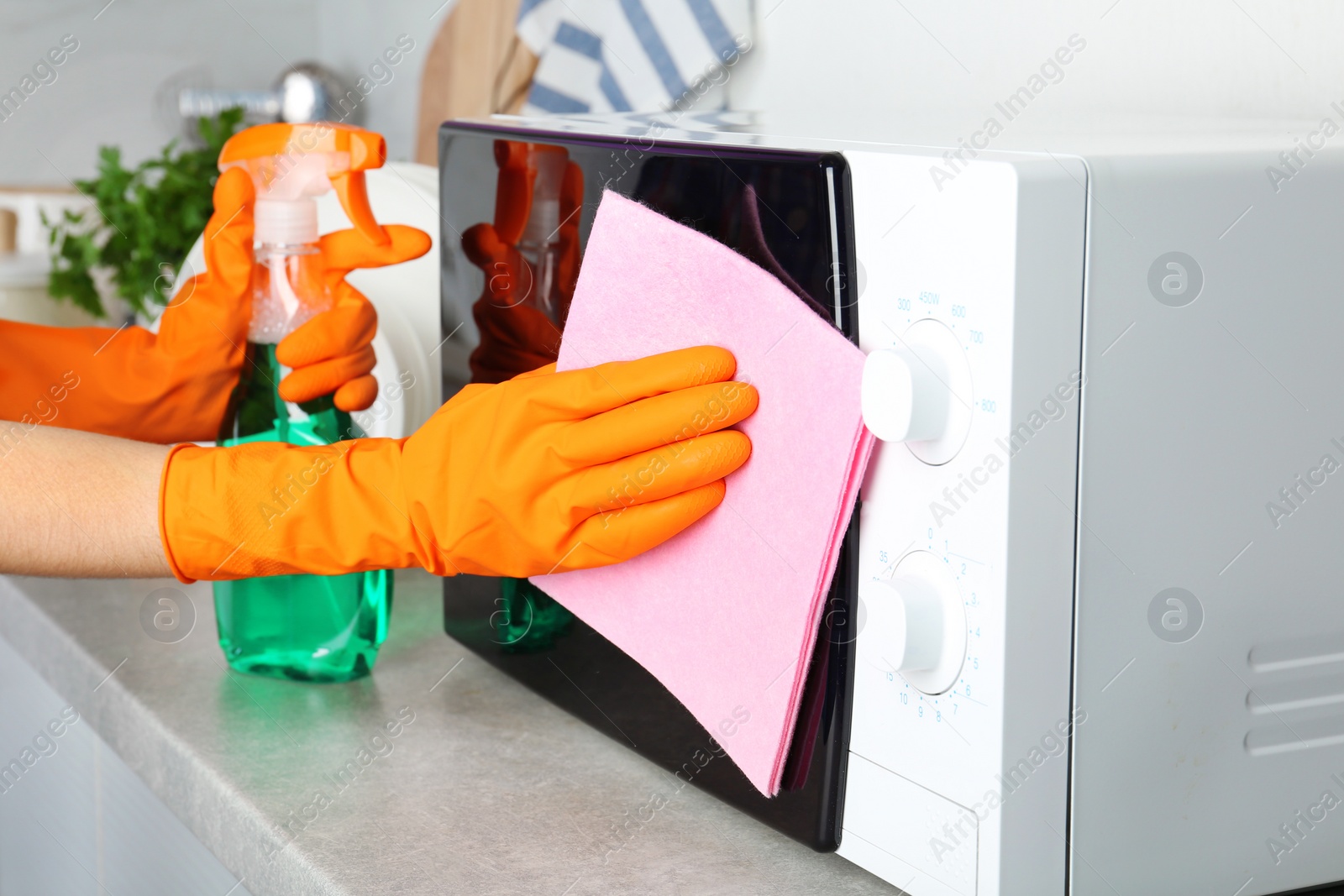 Photo of Woman cleaning microwave oven with rag and detergent in kitchen, closeup