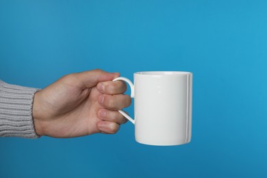 Photo of Man holding white mug on light blue background, closeup