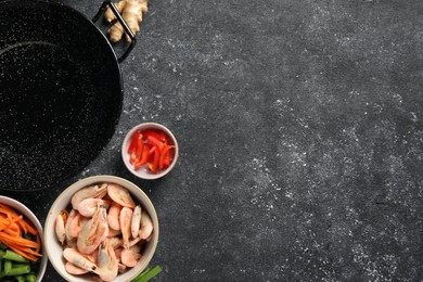 Flat lay composition with black wok and products on dark textured table. Space for text