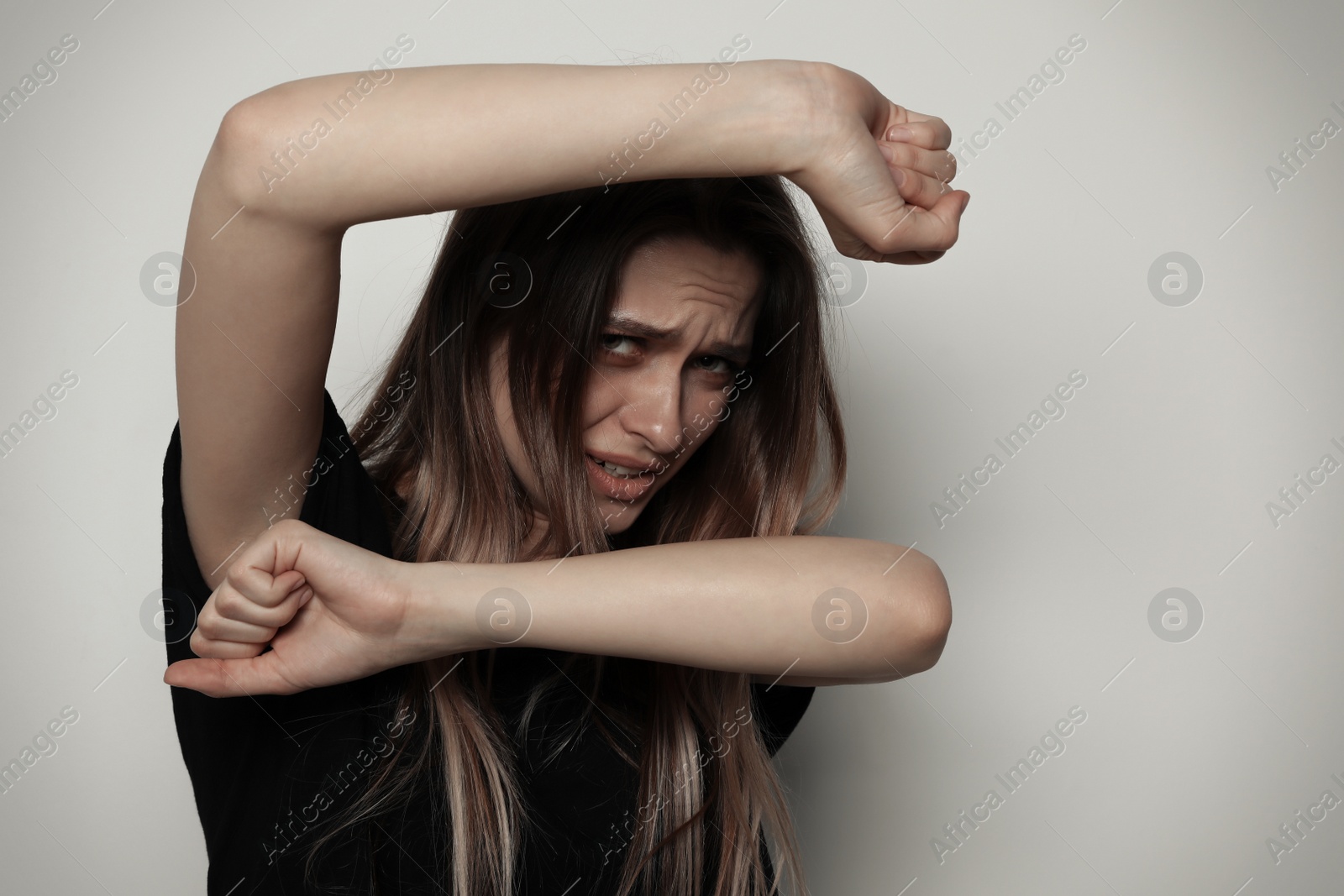 Photo of Portrait of woman protecting herself on light background. Stop violence