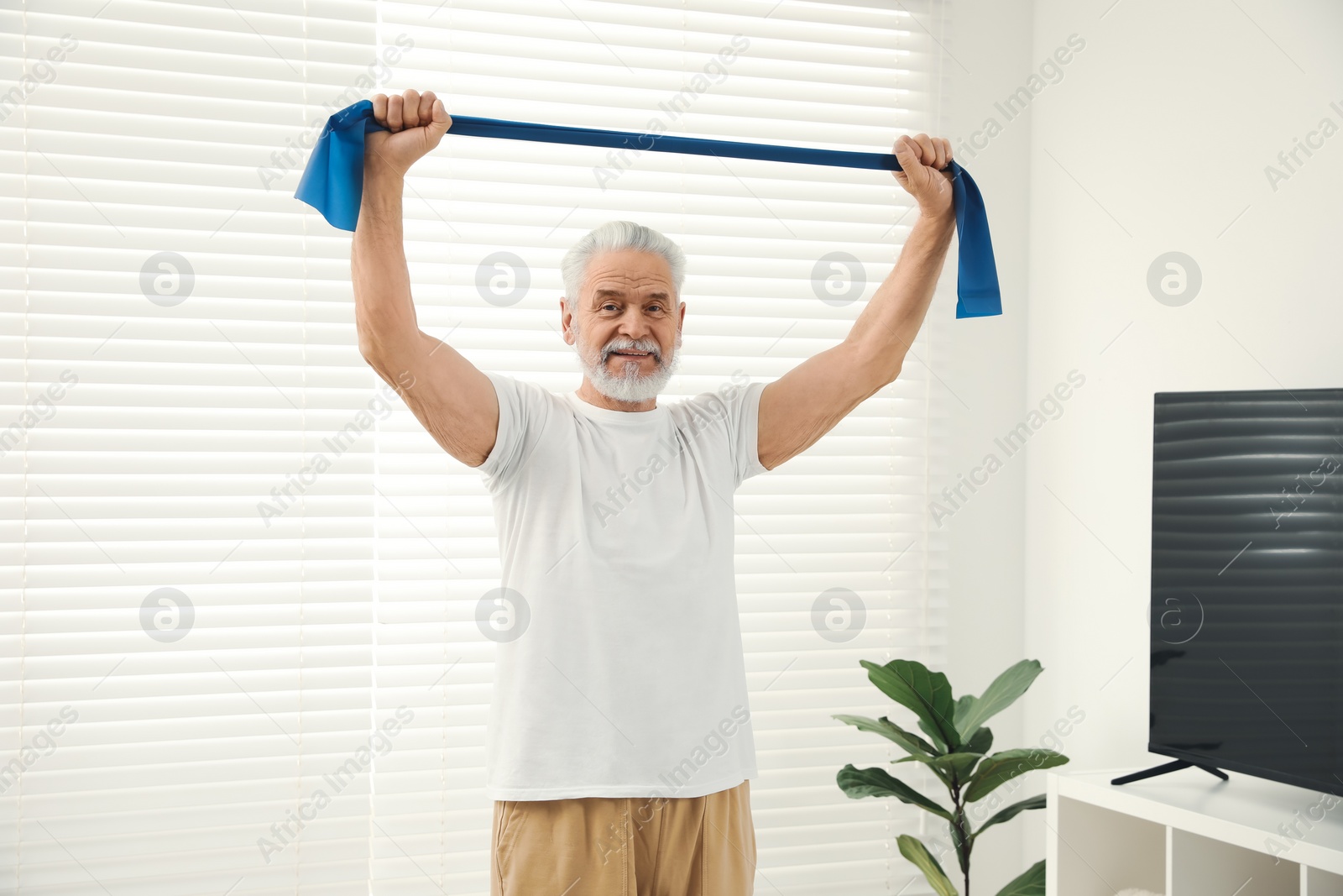 Photo of Senior man doing exercise with fitness elastic band at home