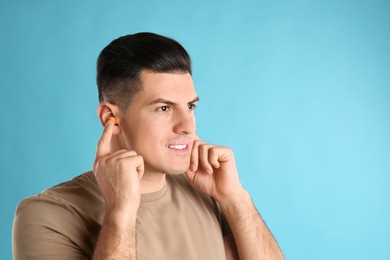 Photo of Man inserting foam ear plugs on light blue background. Space for text