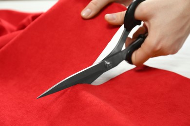 Seamstress cutting red fabric with scissors at workplace, closeup