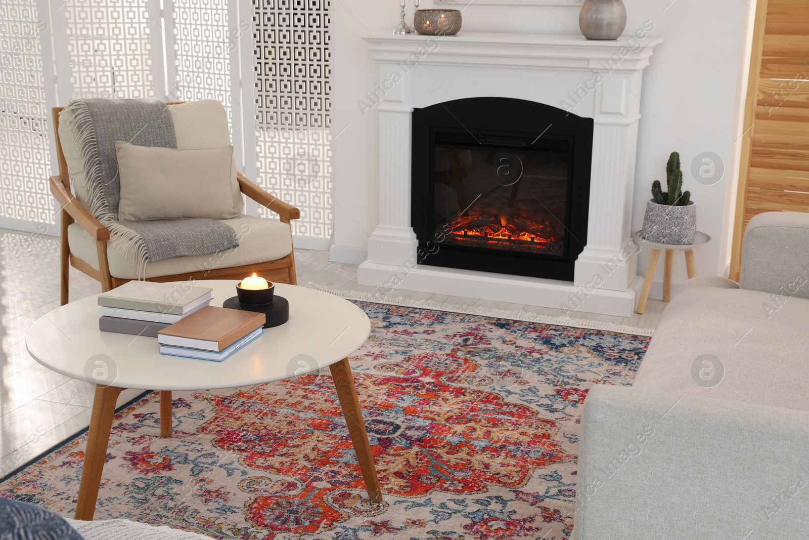 Photo of Beautiful fireplace, armchair and books on table in living room. Interior design