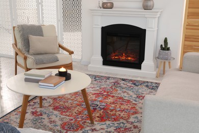 Beautiful fireplace, armchair and books on table in living room. Interior design