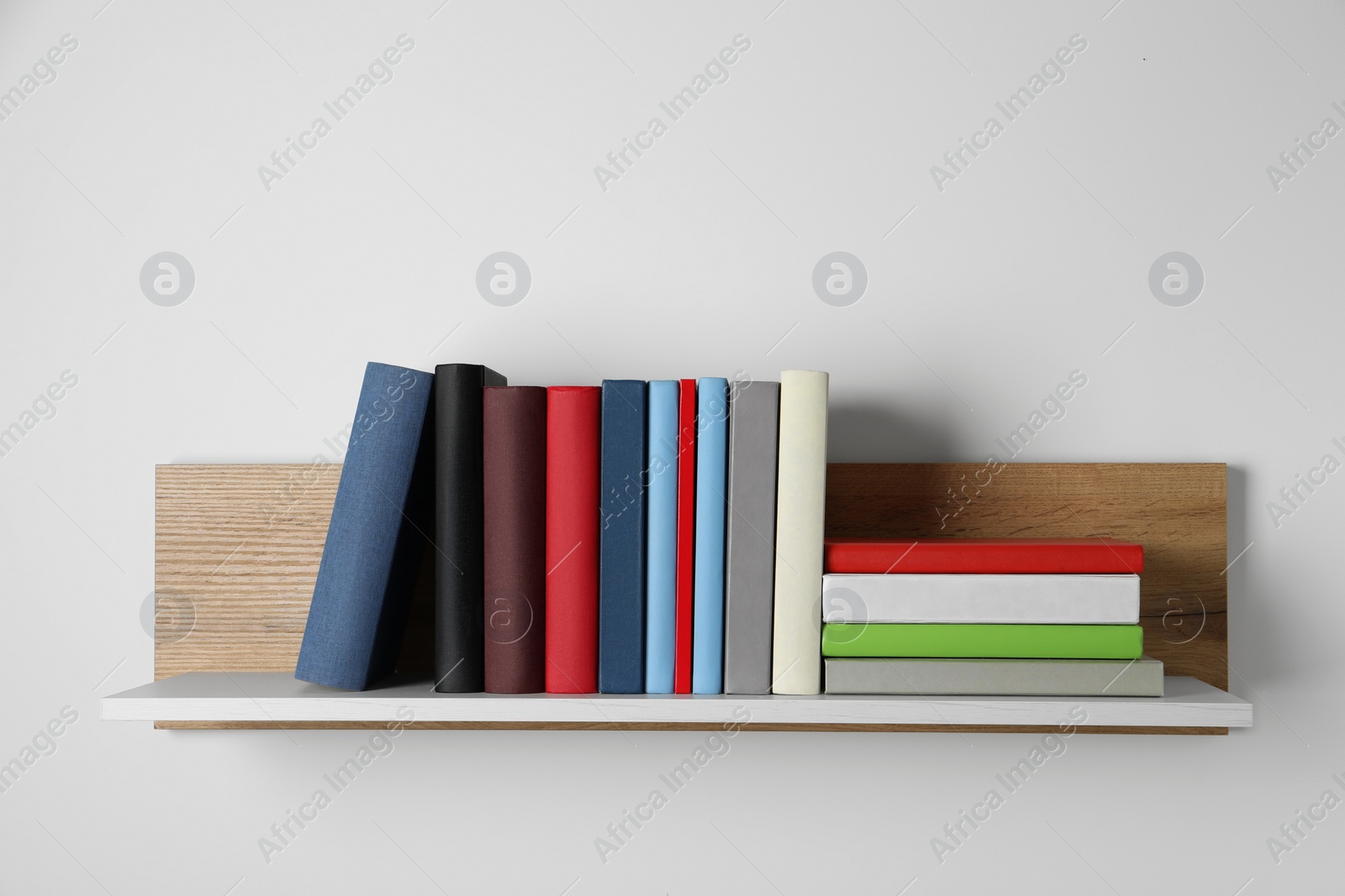 Photo of Many hardcover books on wooden shelf near white wall