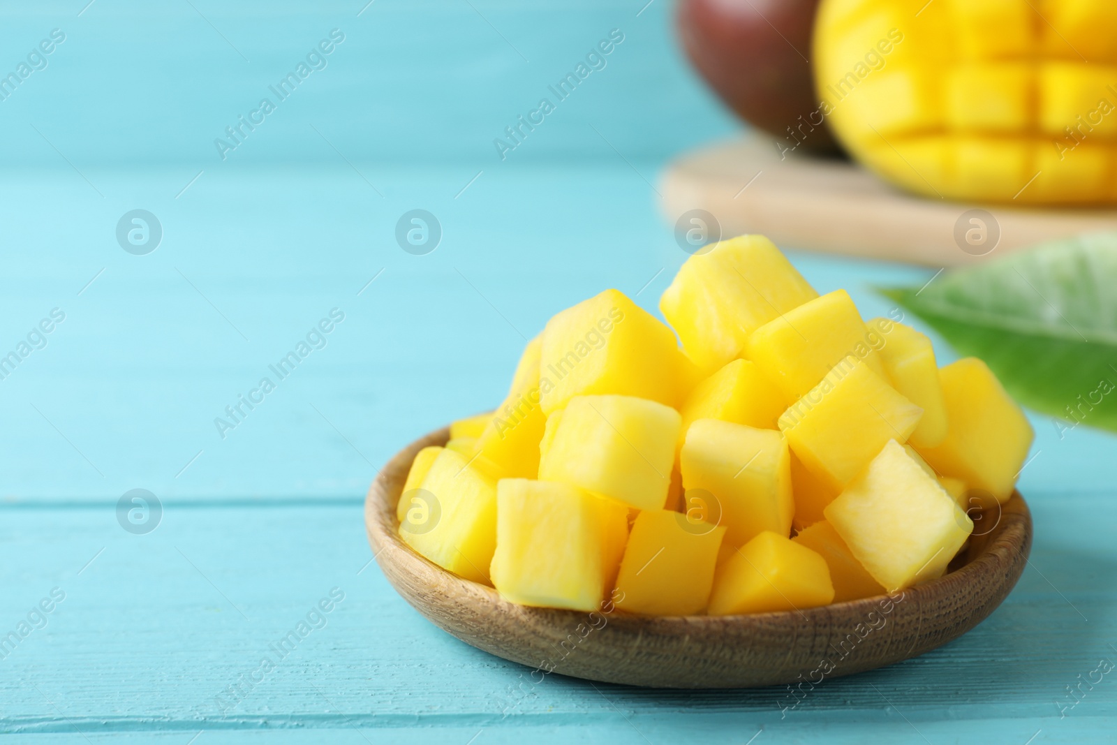 Photo of Cubes of fresh ripe mango on light blue wooden table. Space for text