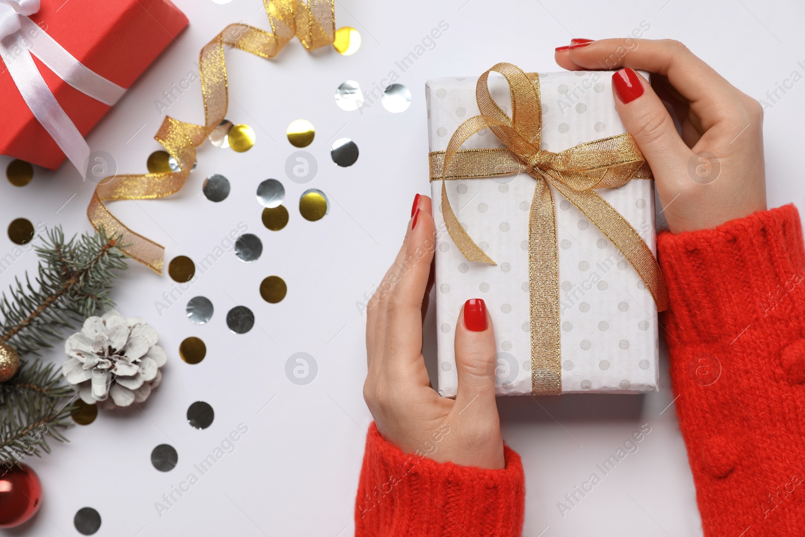 Photo of Woman holding gift box near fir tree branch with Christmas decor on white background, top view