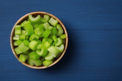 Photo of Bowl of fresh cut celery on blue wooden table, top view. Space for text