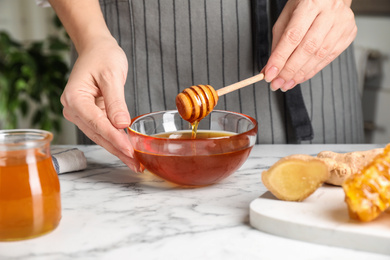 Photo of Woman with tasty honey at marble table, closeup