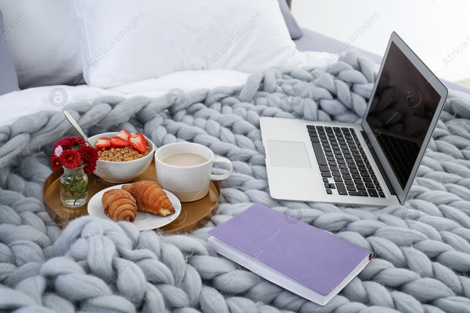 Photo of Laptop, tray with breakfast and notebook on bed. Interior element