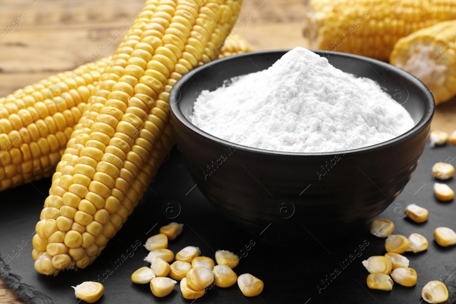 Photo of Bowl with corn starch, ripe cobs and kernels on slate board, closeup