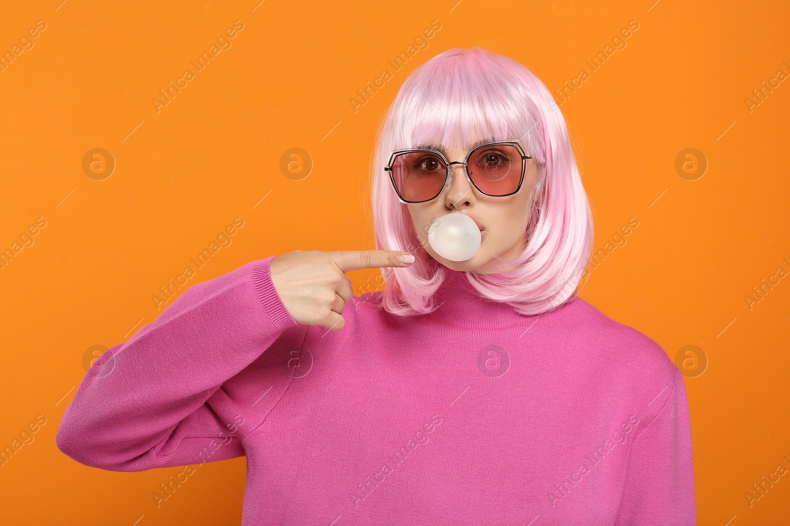 Photo of Beautiful woman in sunglasses blowing bubble gum and pointing at herself on orange background