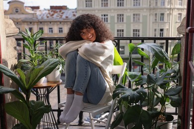 Beautiful young woman relaxing in chair surrounded by green houseplants on balcony