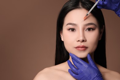 Woman getting facial injection on brown background