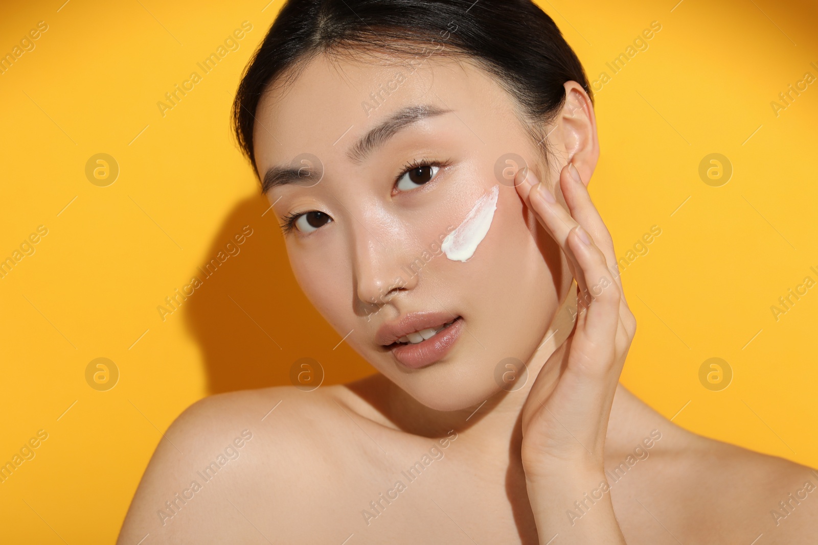 Photo of Beautiful young woman in sunlight with sun protection cream on her face against orange background