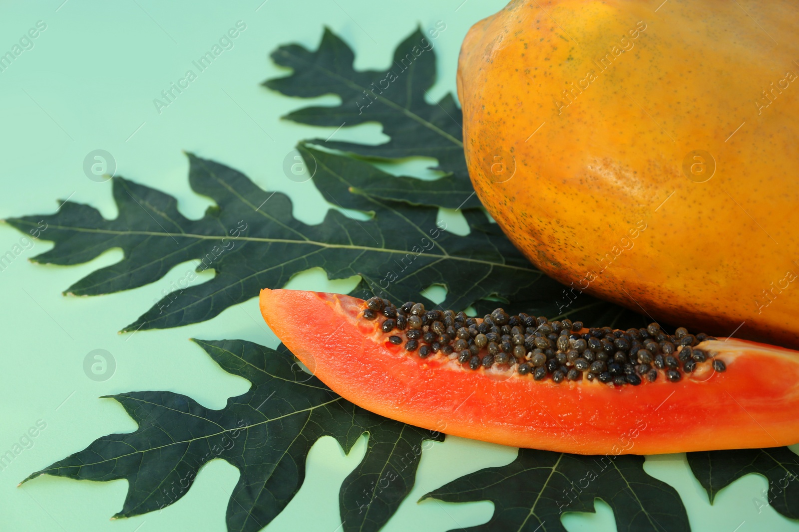 Photo of Whole and cut fresh ripe papaya fruits with leaf on light green background, closeup. Space for text