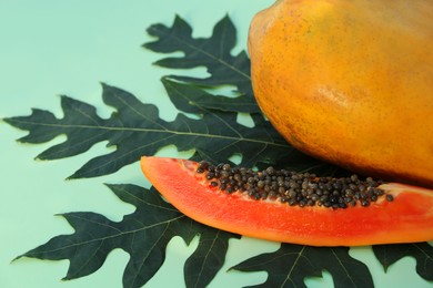 Whole and cut fresh ripe papaya fruits with leaf on light green background, closeup. Space for text