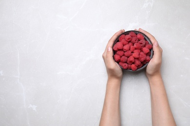 Photo of Woman holding bowl of delicious ripe raspberries at white table, top view. Space for text