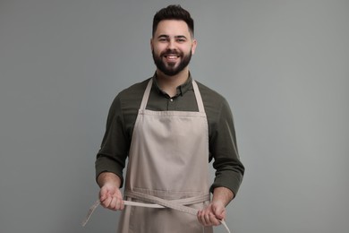 Photo of Smiling man in kitchen apron on grey background. Mockup for design