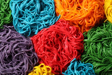 Photo of Rolled spaghetti painted with different food colorings as background, top view