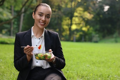 Photo of Lunch time. Happy businesswoman with container of salad on green grass in park, space for text