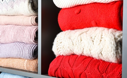 Many knitted winter clothes stacked on shelves, closeup