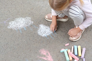 Little child drawing white clouds with chalk on asphalt, closeup