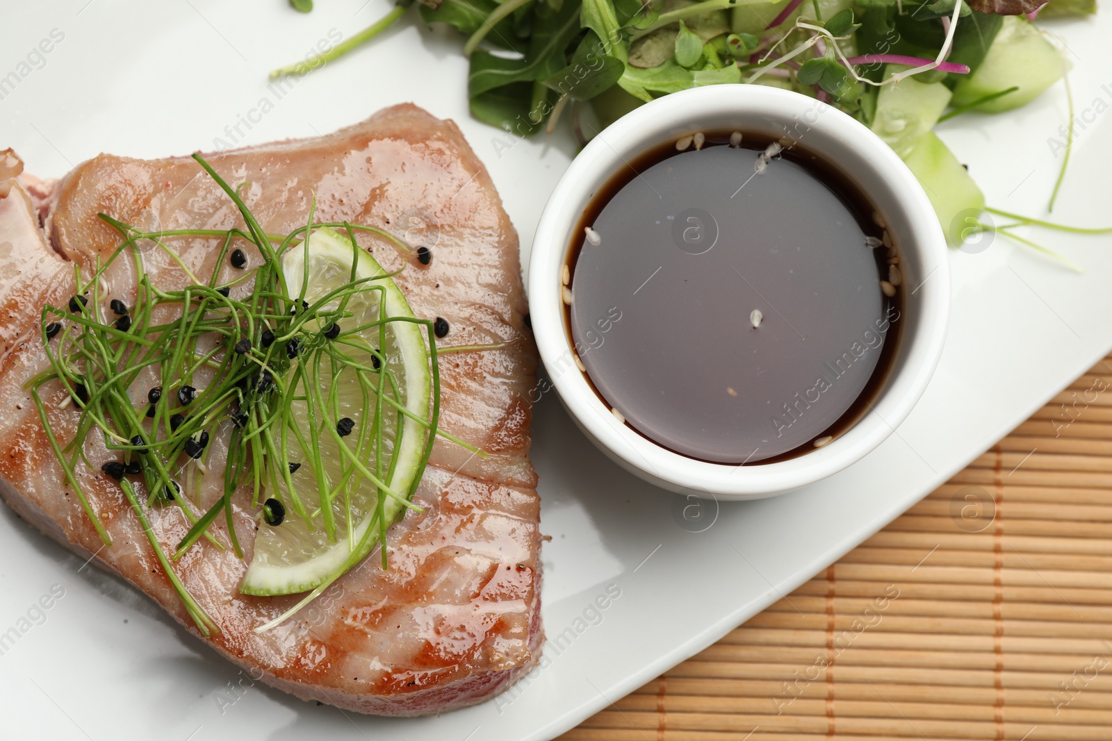 Photo of Delicious tuna steak with salad and sauce on bamboo mat, top view