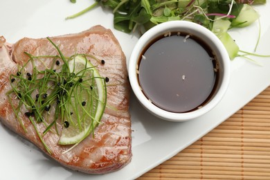 Delicious tuna steak with salad and sauce on bamboo mat, top view