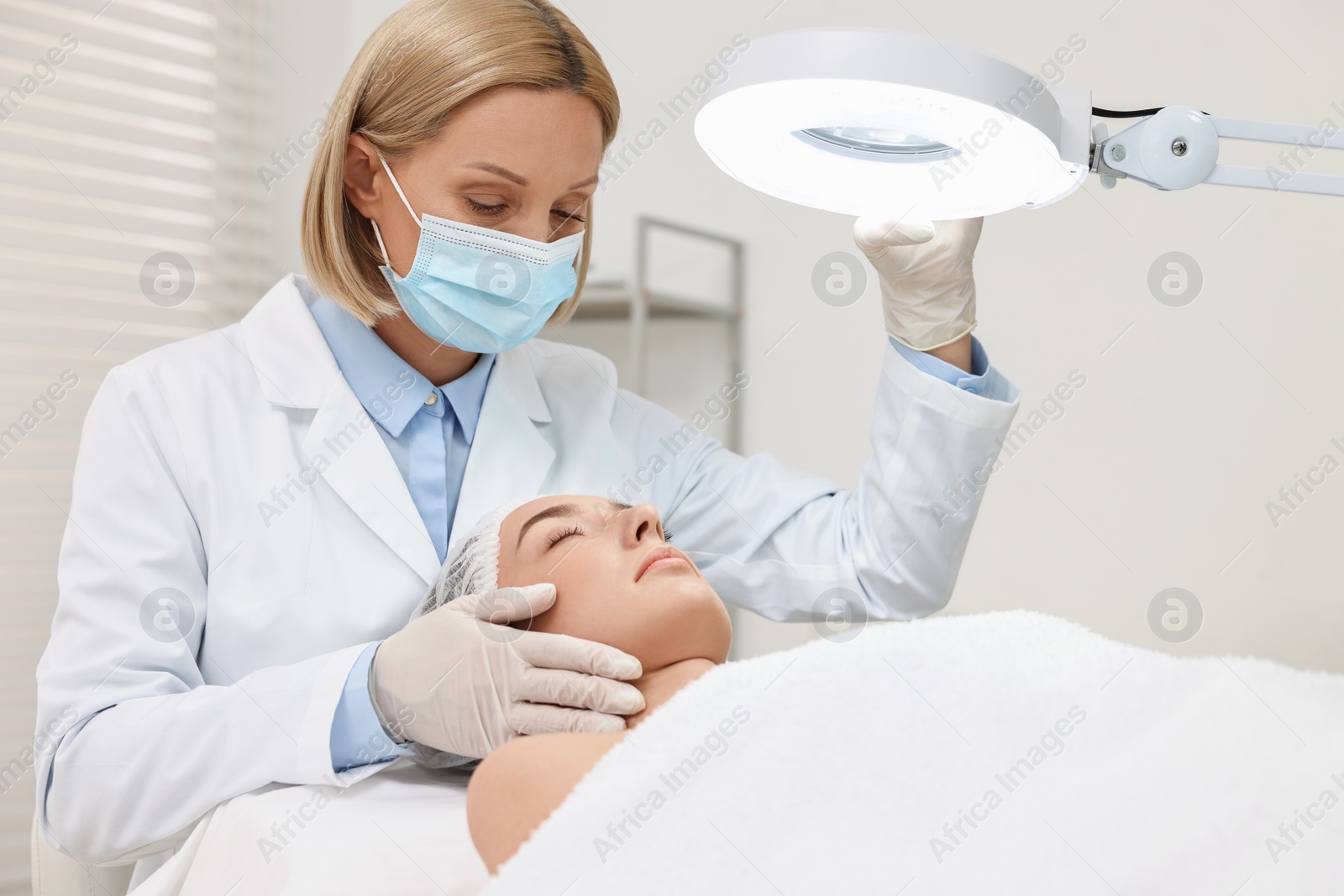 Photo of Dermatologist examining patient`s face under lamp in clinic