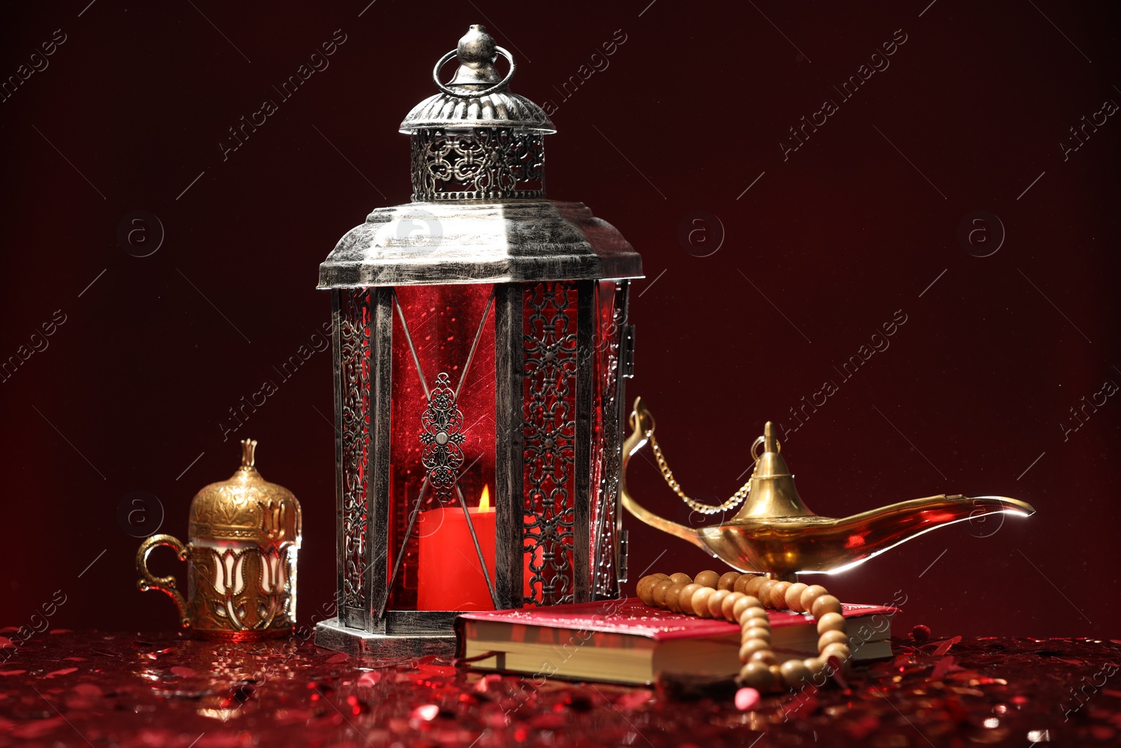 Photo of Arabic lantern, Quran, misbaha and Aladdin magic lamp on shiny red table