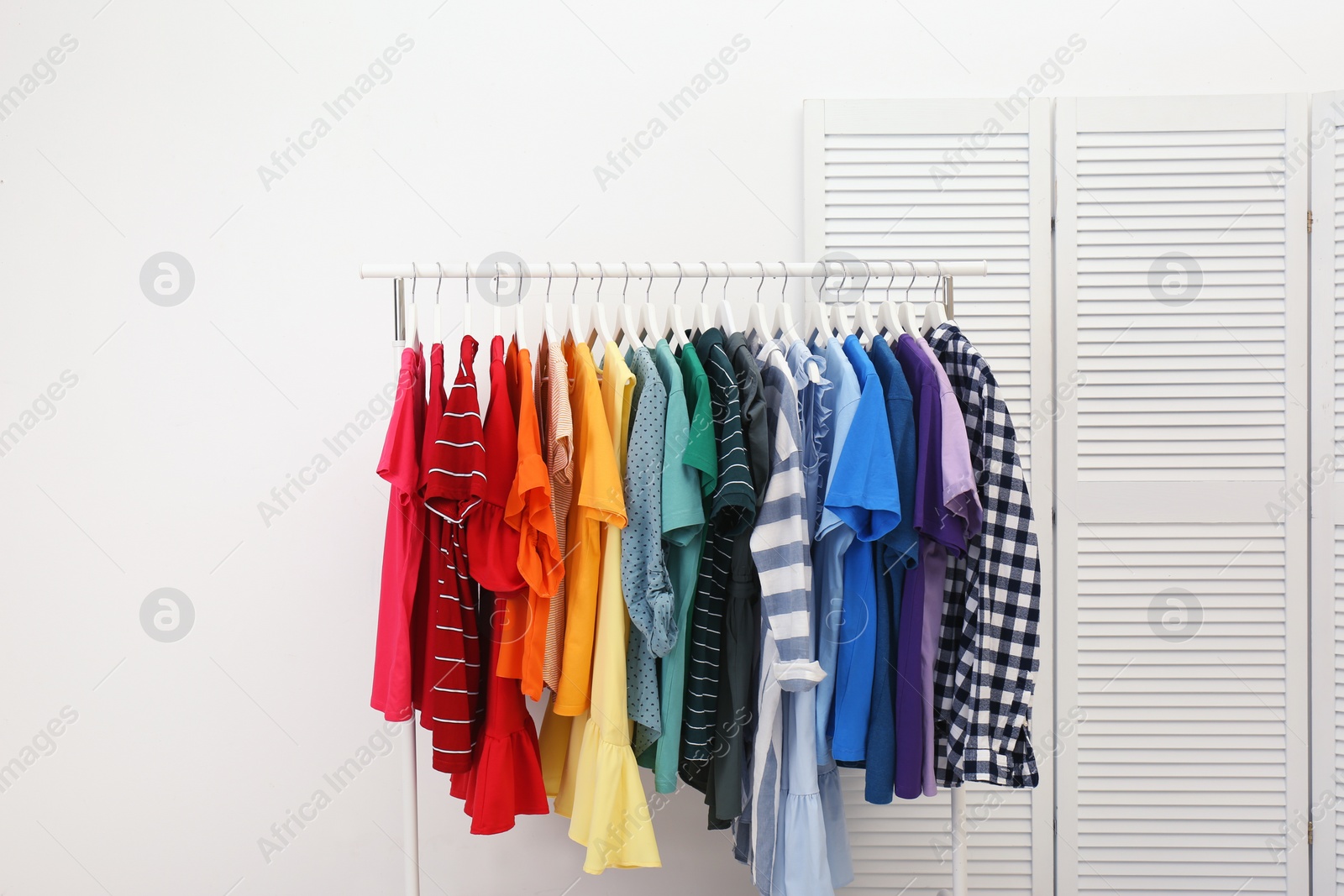 Photo of Rack with bright clothes in room. Rainbow colors