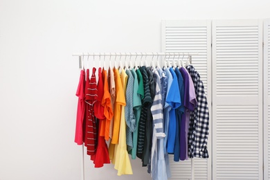 Rack with bright clothes in room. Rainbow colors