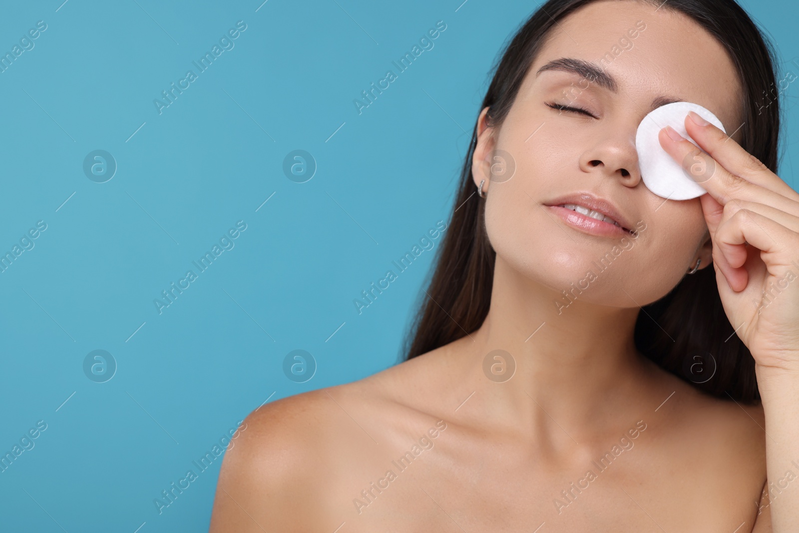 Photo of Young woman with cotton pad on light blue background. Space for text