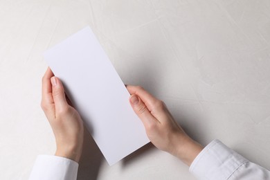 Woman holding blank card at white table, top view. Mockup for design