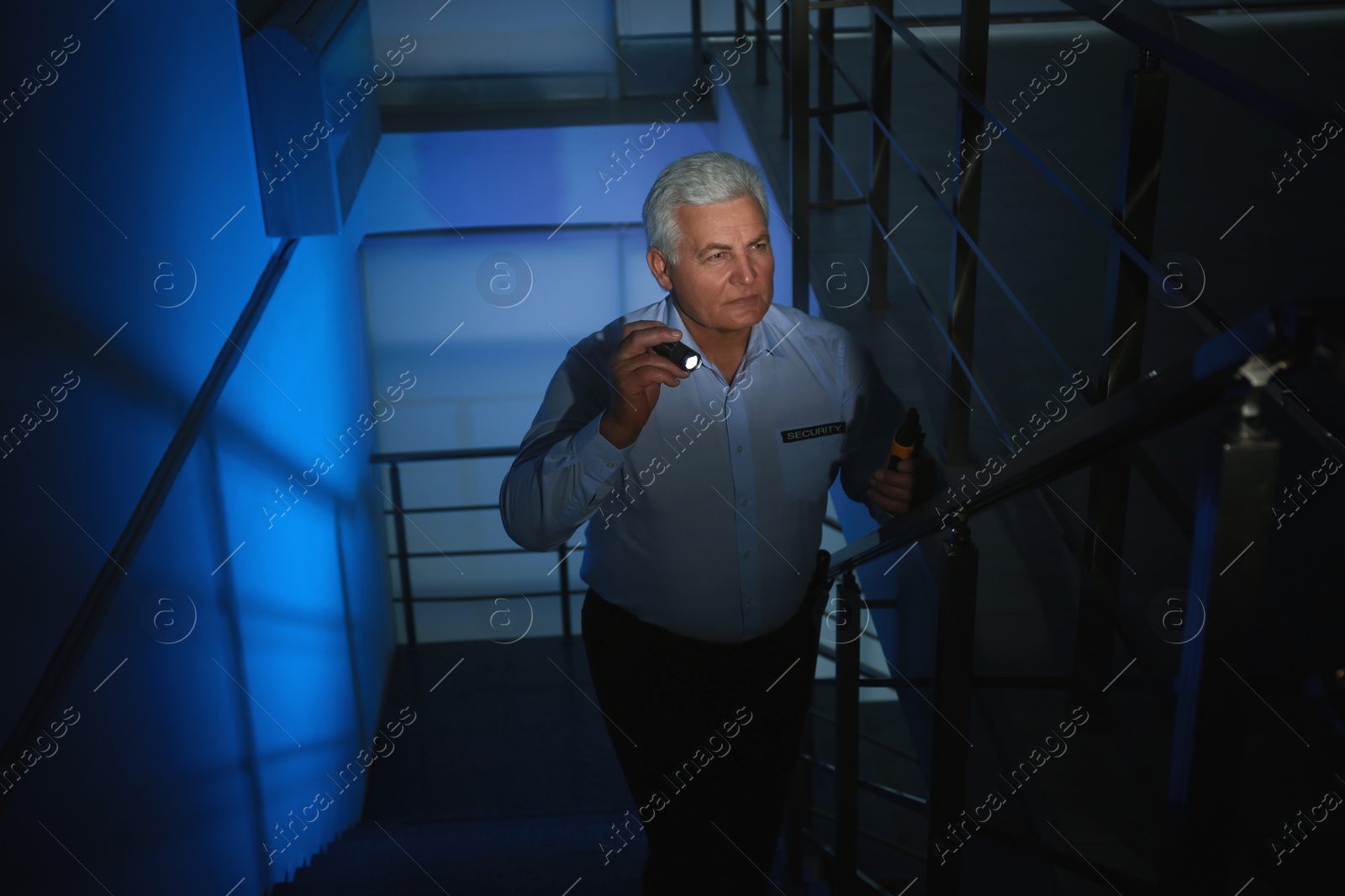 Photo of Professional security guard with flashlight on stairs in dark room