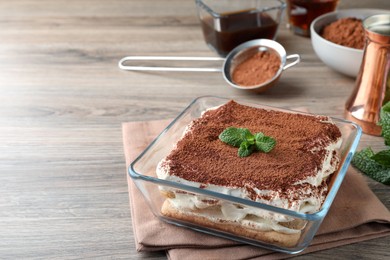 Photo of Glass bowl with delicious tiramisu cake on wooden table, space for text