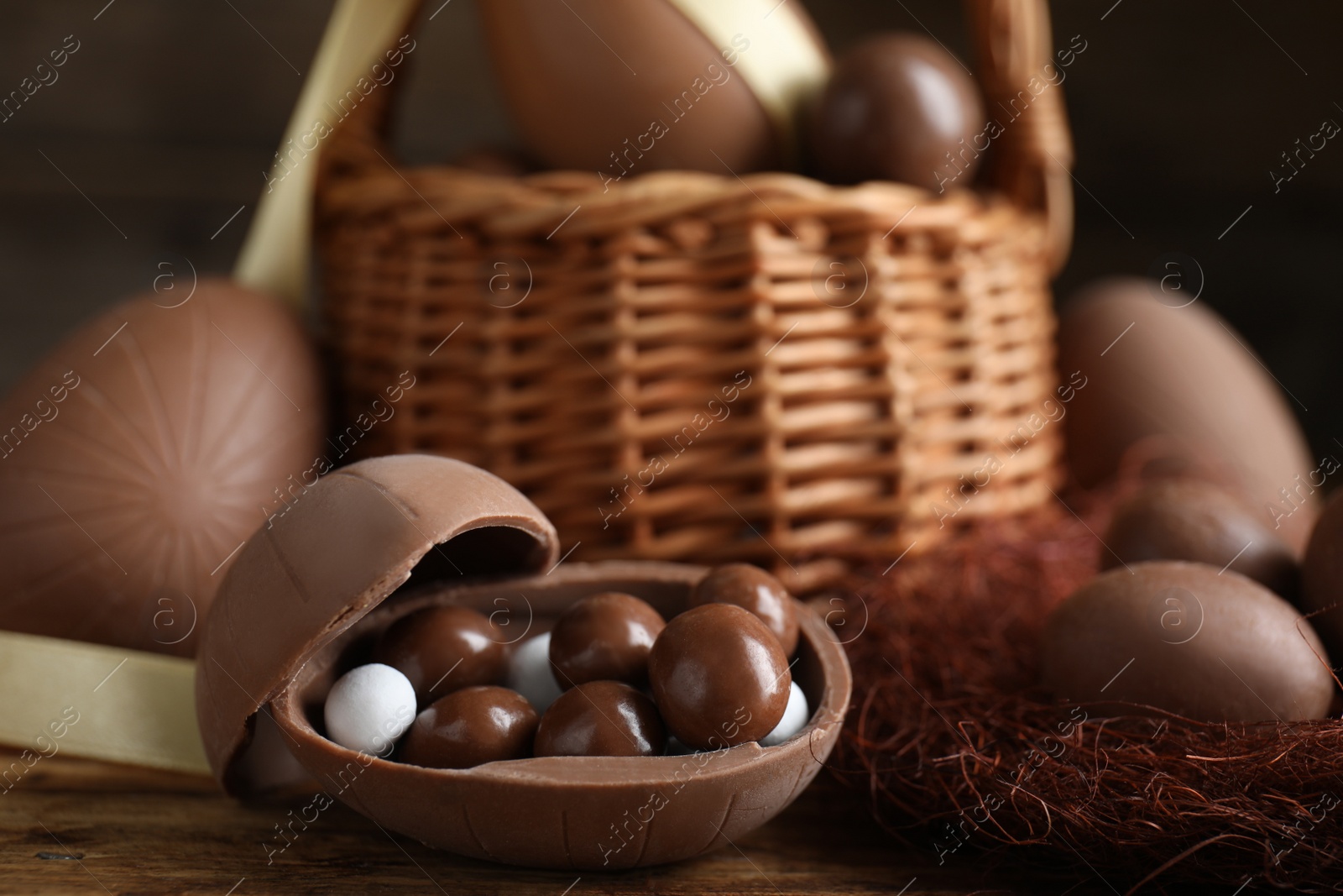 Photo of Tasty chocolate egg with candies on wooden table, closeup. Space for text