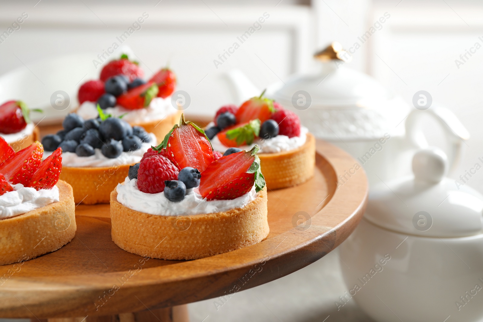 Photo of Cake stand with different berry tarts on table. Delicious pastries