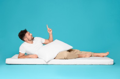 Photo of Man with pillow on soft mattress pointing upwards against light blue background