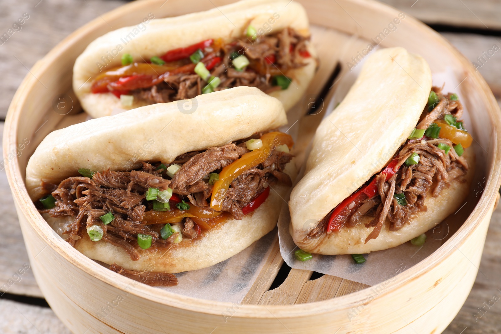 Photo of Delicious gua bao in bamboo steamer on wooden table, closeup