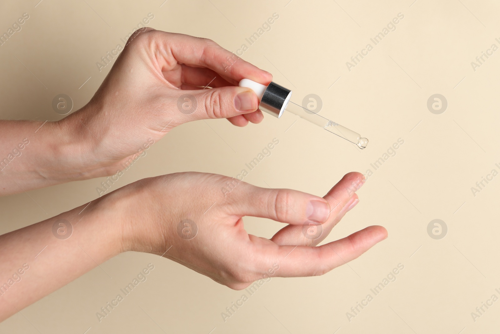 Photo of Woman applying cosmetic serum onto finger on beige background, closeup