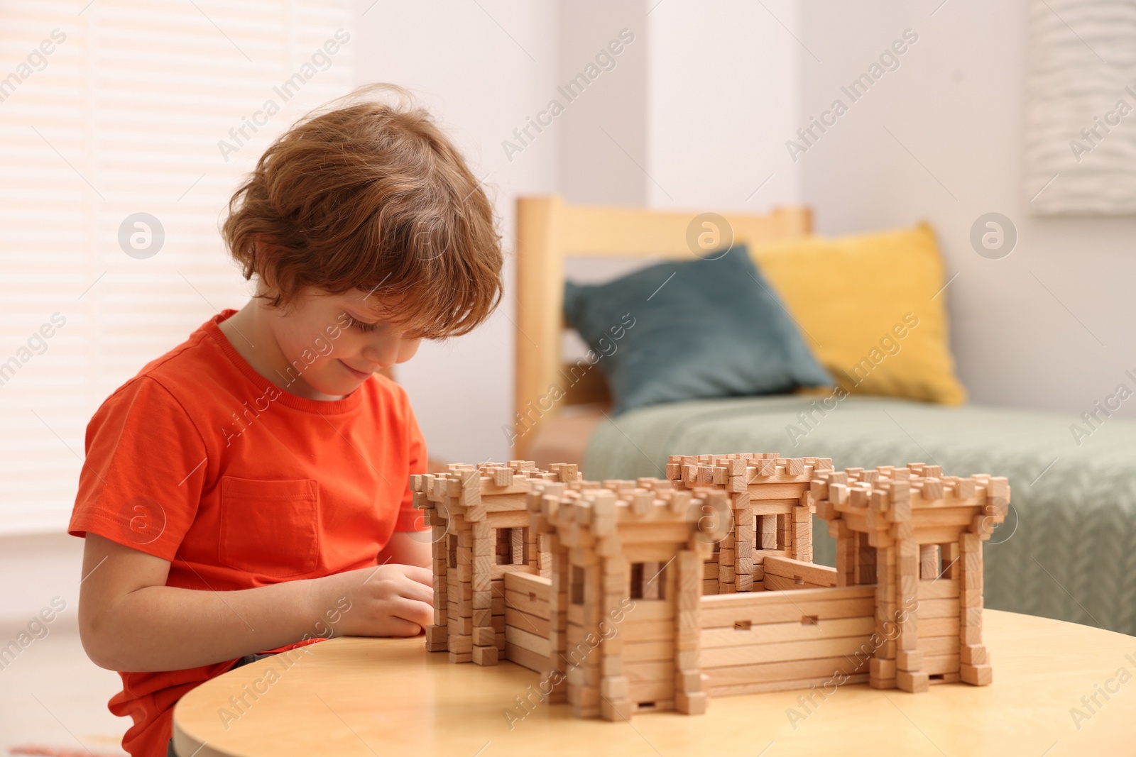 Photo of Cute little boy playing with wooden fortress at table in room. Child's toy