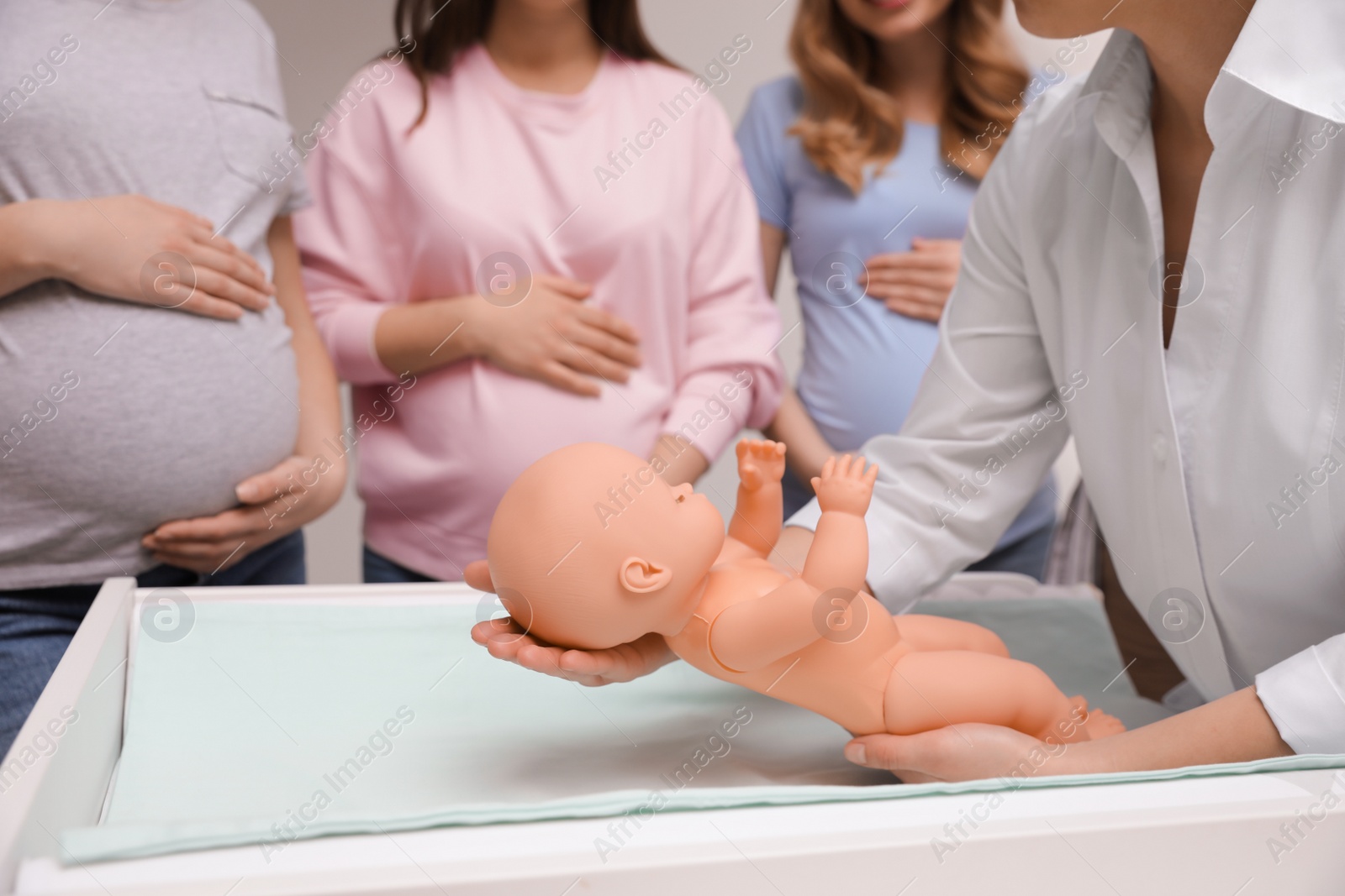 Photo of Pregnant women learning how to swaddle baby at courses for expectant mothers indoors, closeup