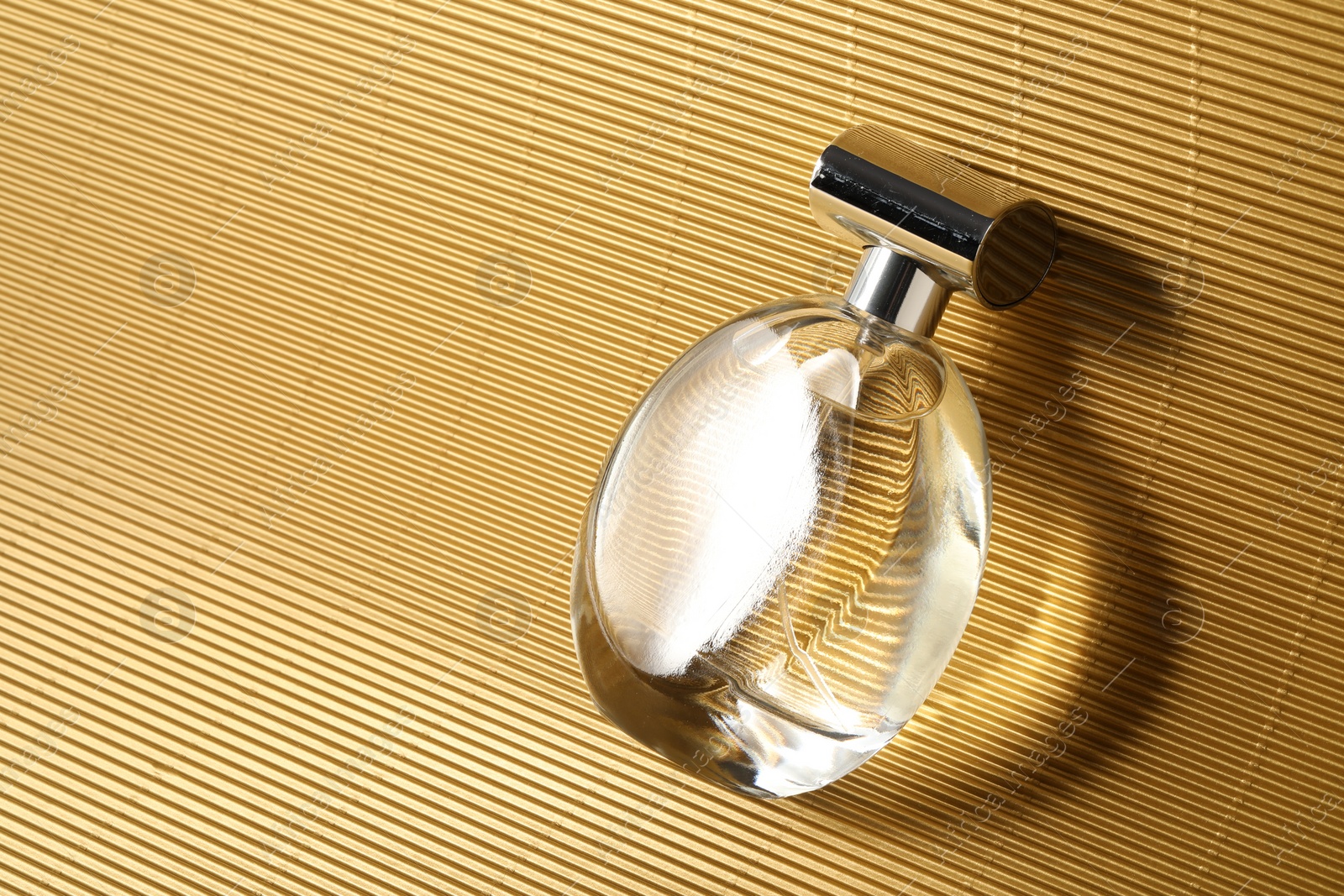 Photo of Luxury women's perfume. Sunlit glass bottle on golden surface, top view. Space for text