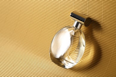 Luxury women's perfume. Sunlit glass bottle on golden surface, top view. Space for text