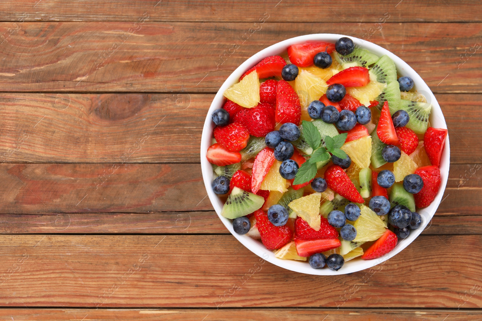 Photo of Delicious fresh fruit salad in bowl on wooden table, top view. Space for text