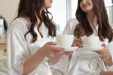 Photo of Bride and her bridesmaid with cups of tea at home, closeup. Wedding day